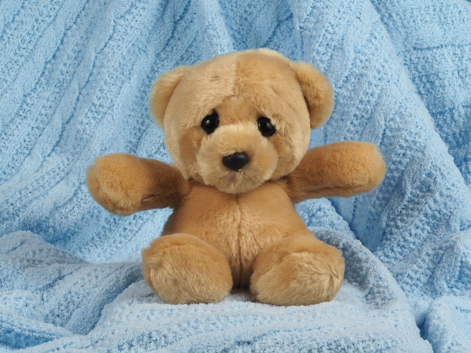 A soft teddy bear sitting on a light blue knitted blanket