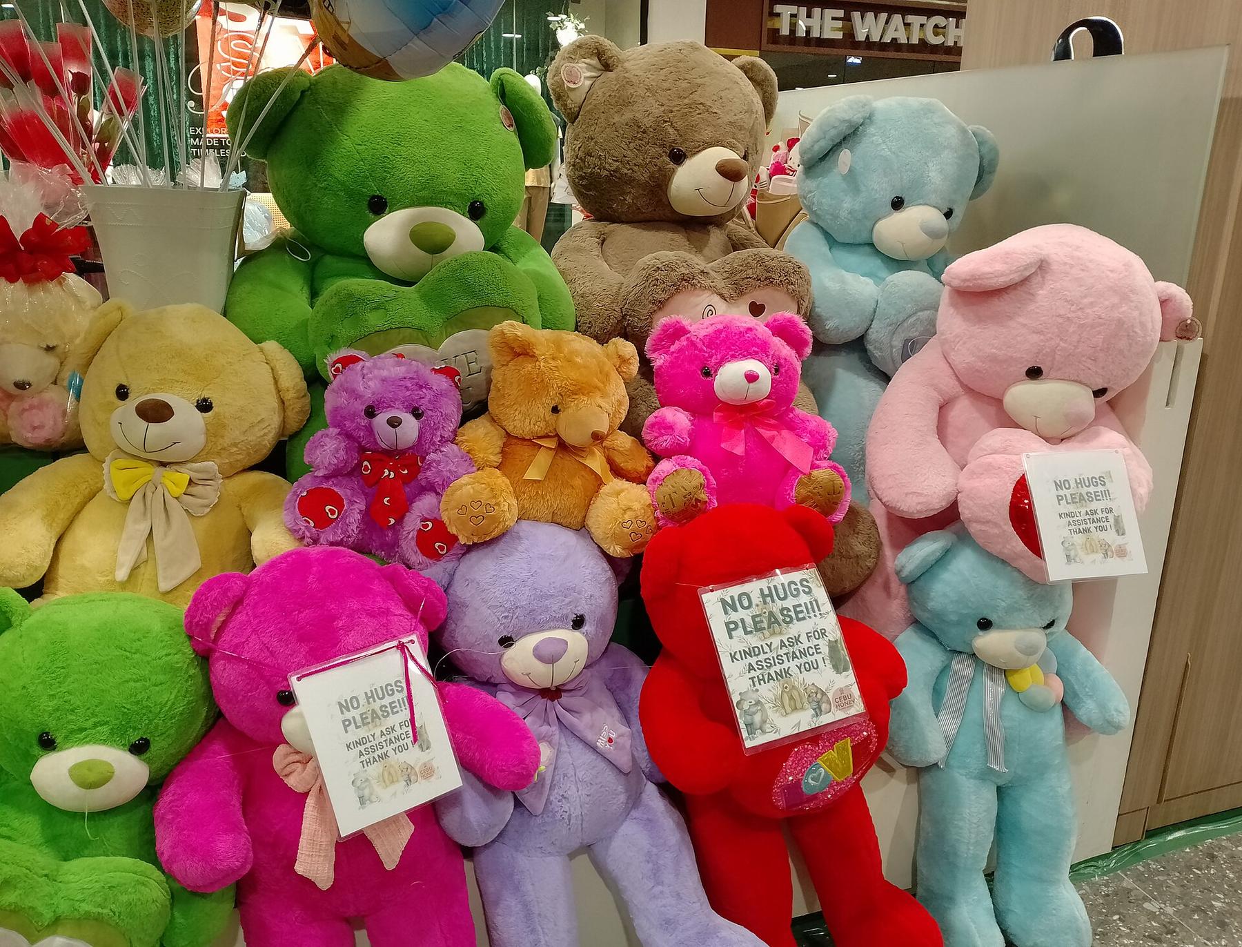 A wall of colourful teddy bears in pink, green, blue and brown stacked on a shop display