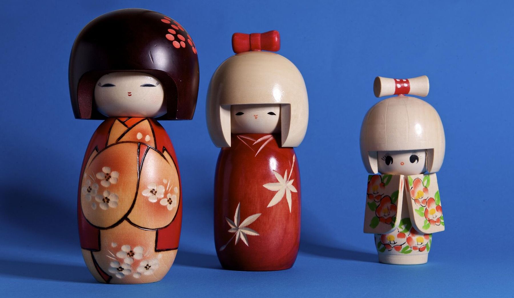 Three painted wooden kokeshi dolls lined up against a blue backdrop